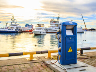 Charging station for boats, electrical outlets to charge ships in harbor - supply electricity for recharging of battery on shore in marina jetty. Electrical power sockets bollard point on pier near sea coast. Luxury yachts docked in port at sunset.