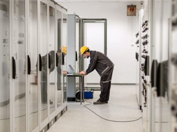 Field service engineer inspect relay protection system with laptop computer. Bay control unit. Medium voltage switchgear